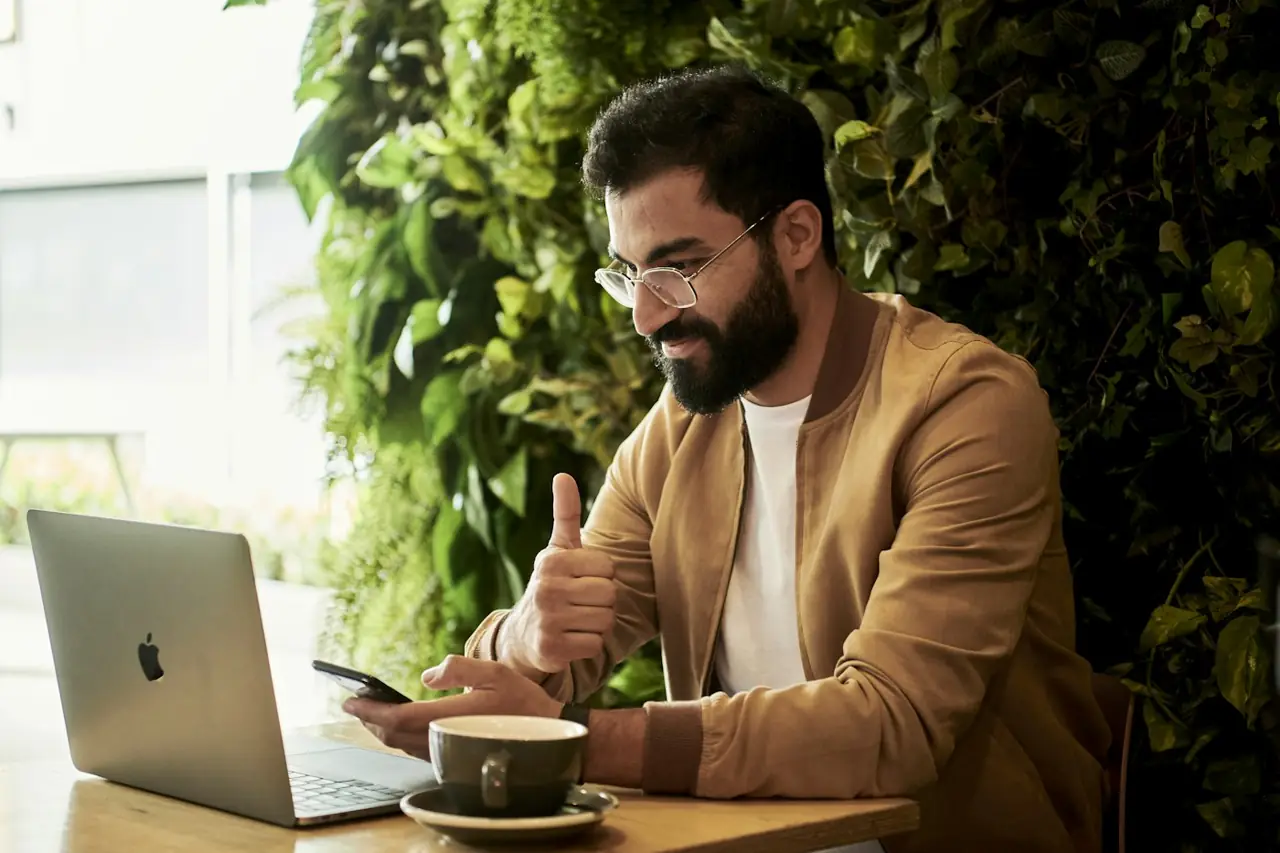 A business owner smiling at his laptop at an outdoor table with a coffee