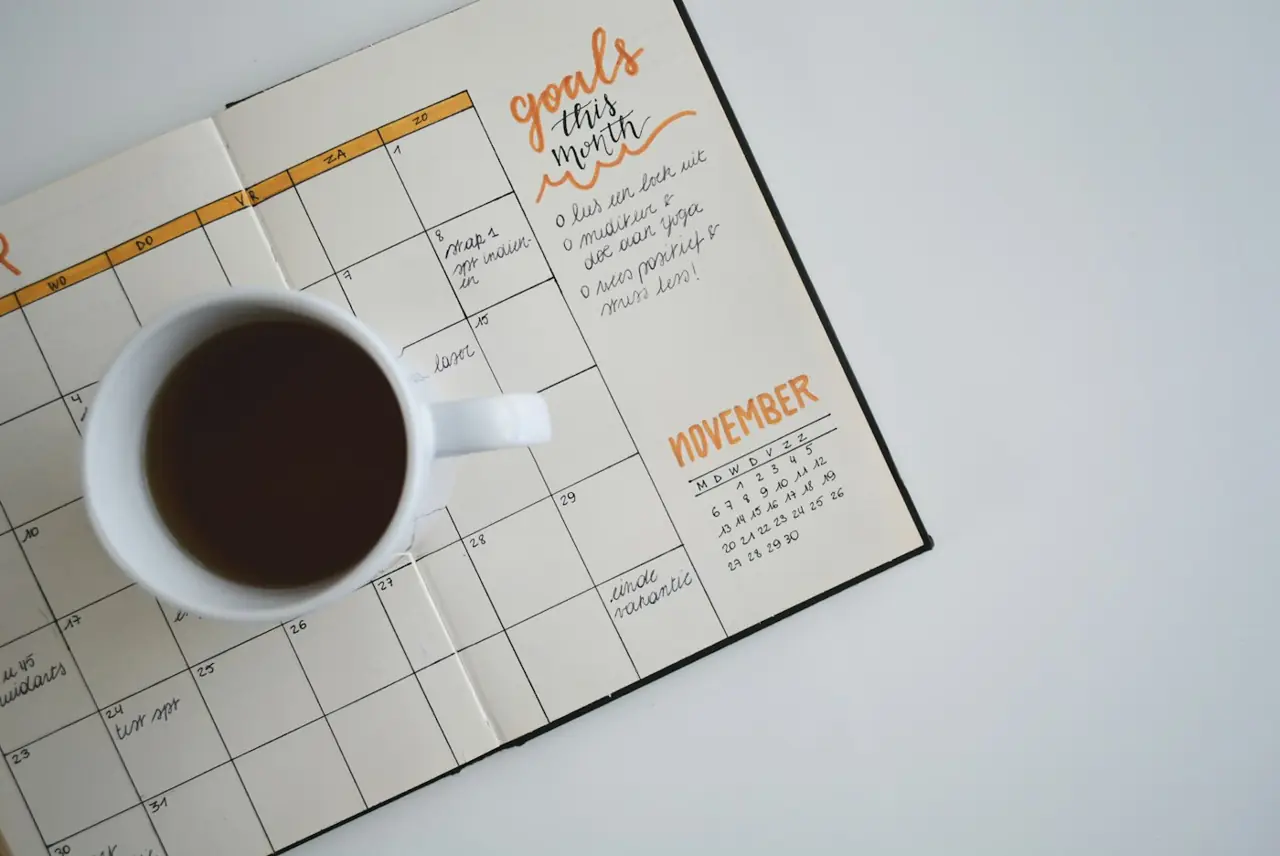 A paper planner open to a busy week next to a cup of black coffee