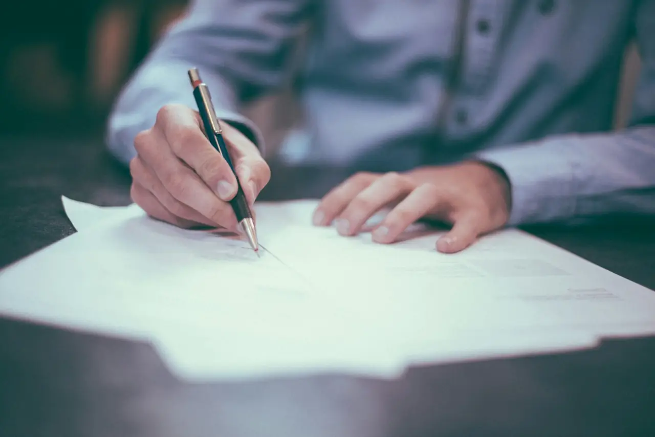 A person signing a printed contract at a desk